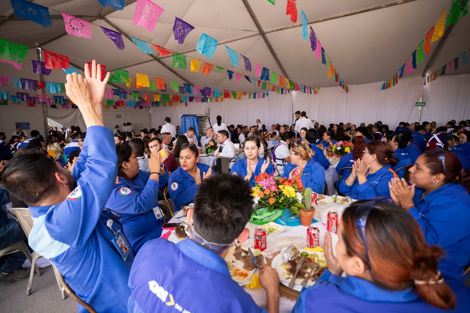 A festive celebration in a decorated room with colorful banners and people in blue uniforms cheering and raising their hands.
