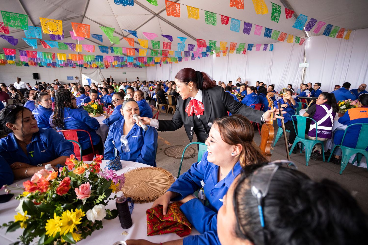 Students in blue uniforms gather at decorated tables under colorful flag banners during a festive celebration event.