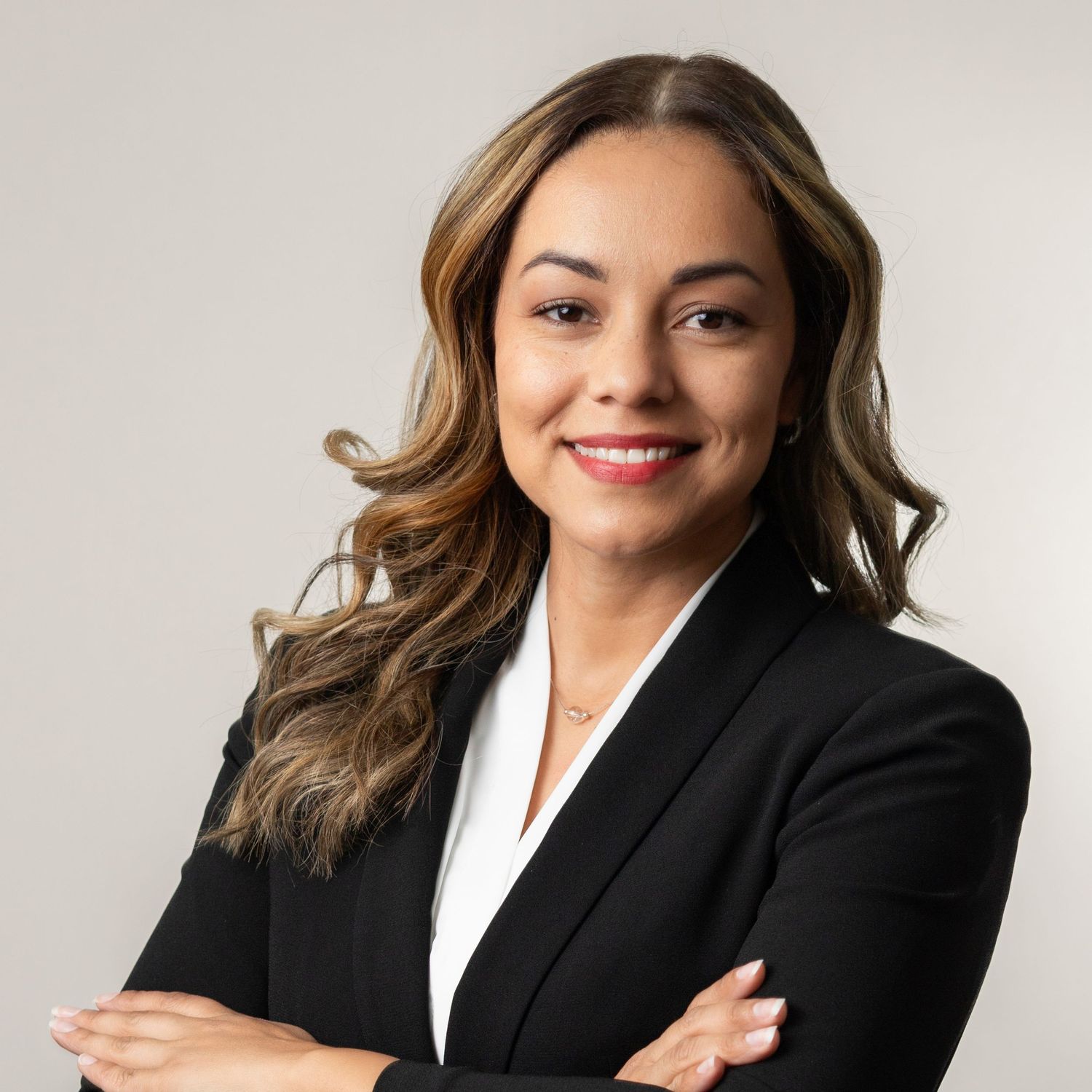 Professional business portrait of someone in a black blazer and white shirt smiling against a light background.