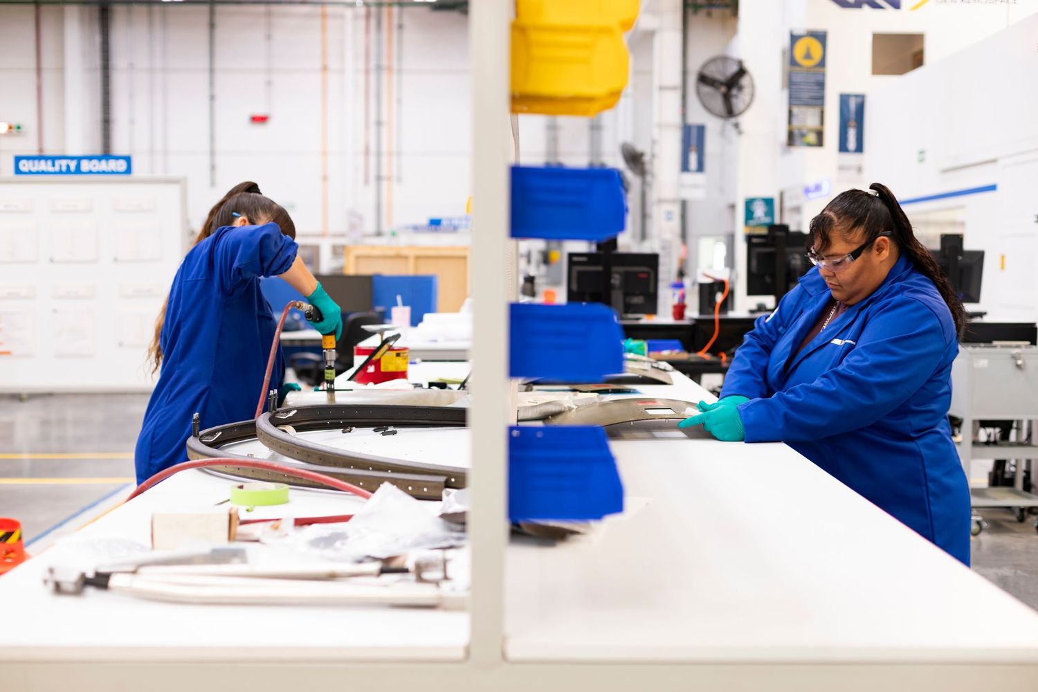 Laboratory technicians in blue coats work at clean white stations performing scientific research and testing procedures.