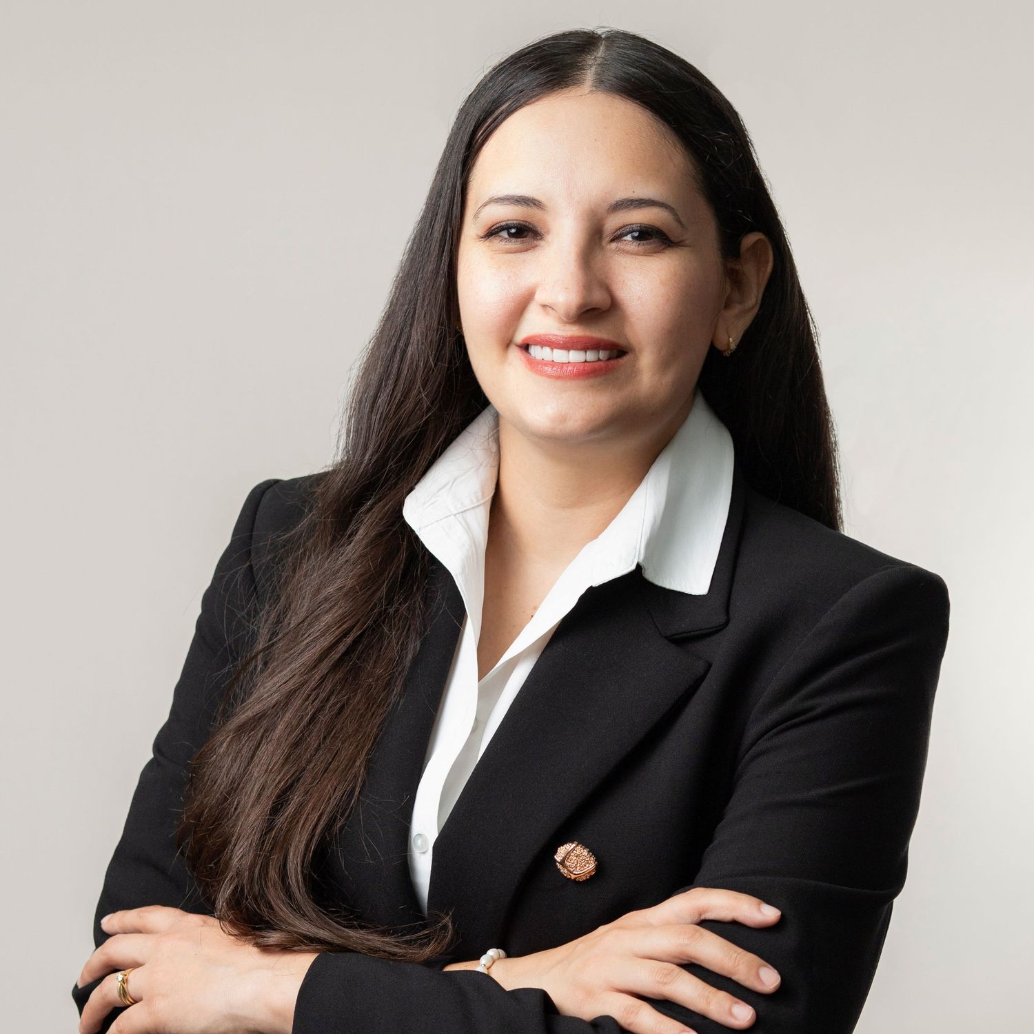 Professional headshot of a person in business attire with long dark hair and a black blazer smiling at the camera.