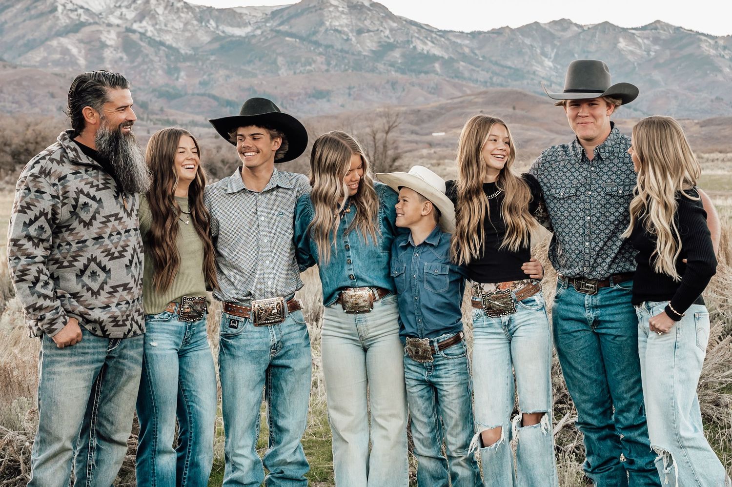 Group wearing denim poses together against mountain backdrop in casual western style.