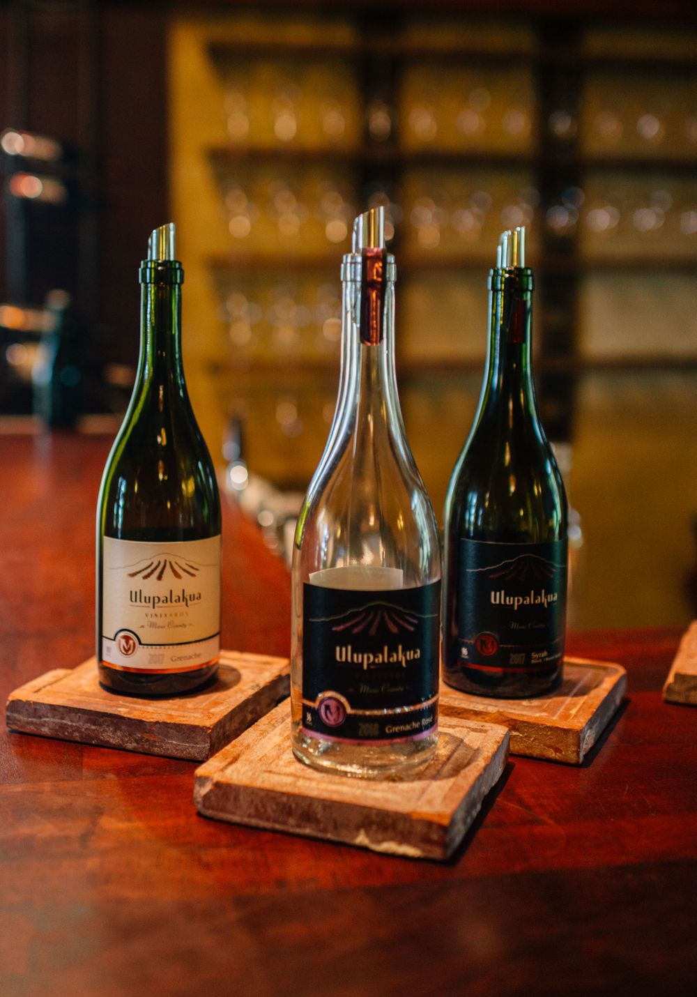 Wine bottles displayed on wooden coasters along a bar counter.