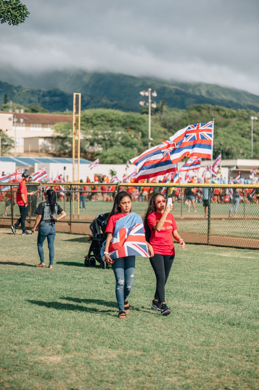 People walking across a grass field carrying Hawaiian state flags.