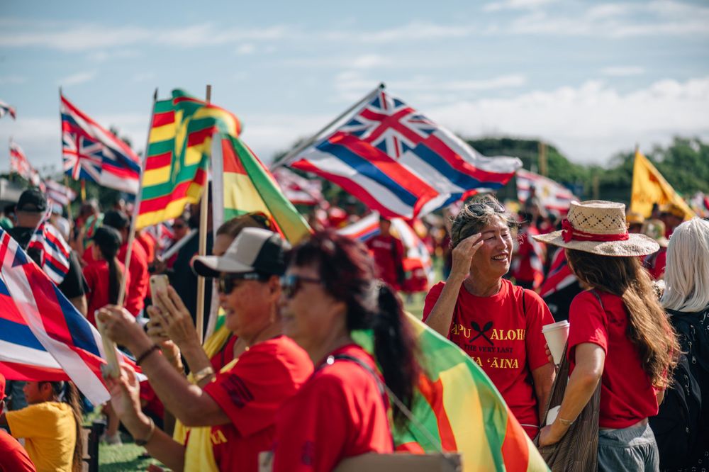Large crowd waving Hawaiian state flags at an outdoor rally event on a sunny day.