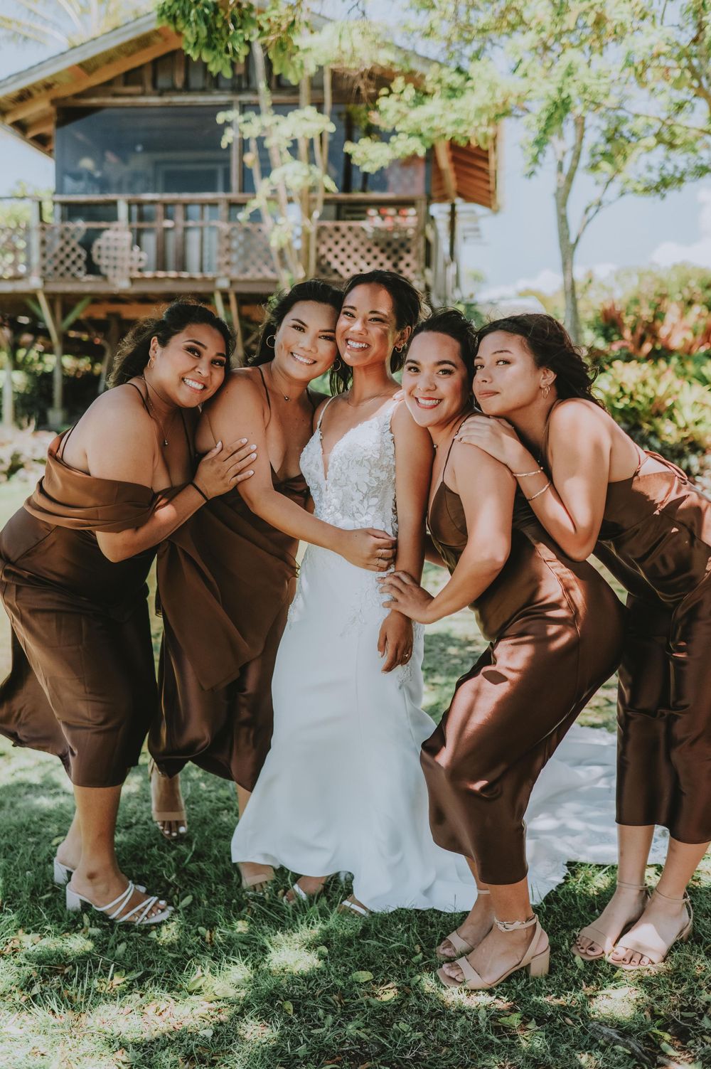 Bridesmaids in brown dresses pose playfully together on grass in a candid wedding photo series.