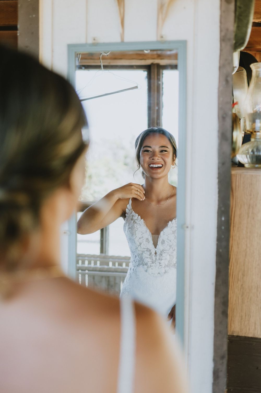 Bride laughing while looking at herself in mirror during wedding preparations.