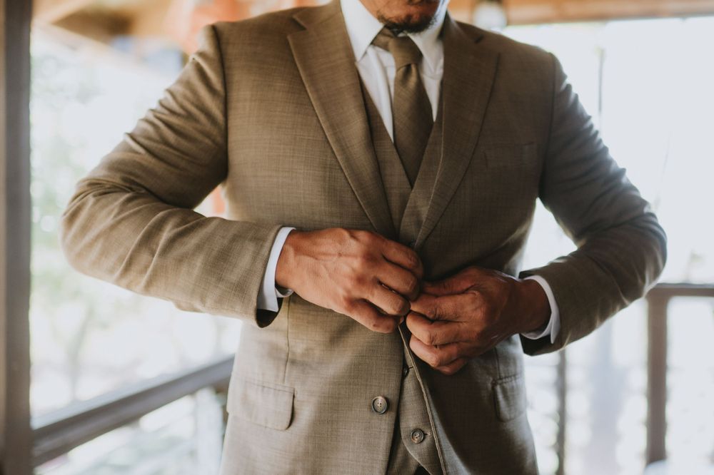 Groomsmen in tan suits adjust their ties and cufflinks while getting ready for a wedding ceremony.