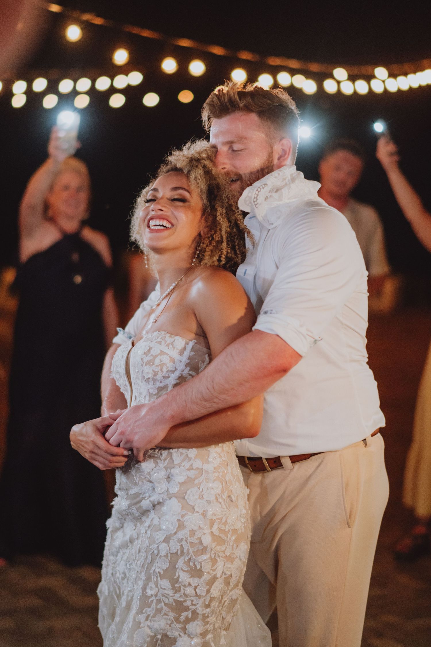 A joyful evening wedding dance under string lights on the beach.