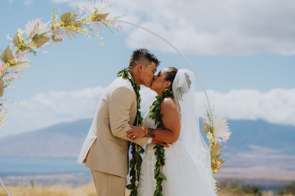 Intimate wedding moment under floral arch with mountains in background.