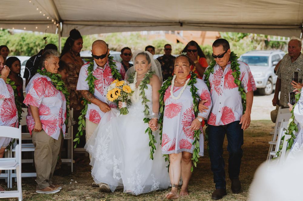 Wedding celebration under white tent with floral decorations and gathered guests.