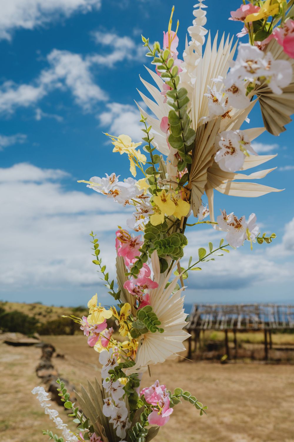 Tropical floral arch with white and pink flowers against a blue sky and desert landscape.