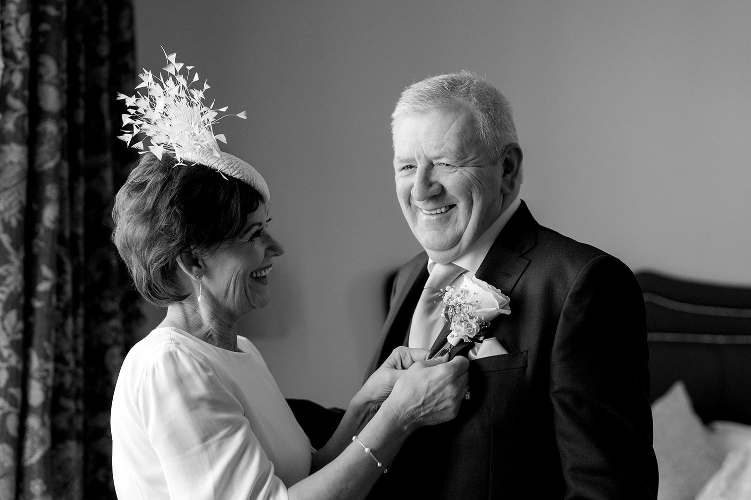 A heartwarming black and white photo capturing a joyful moment as a couple shares a laugh while adjusting boutonnieres.
