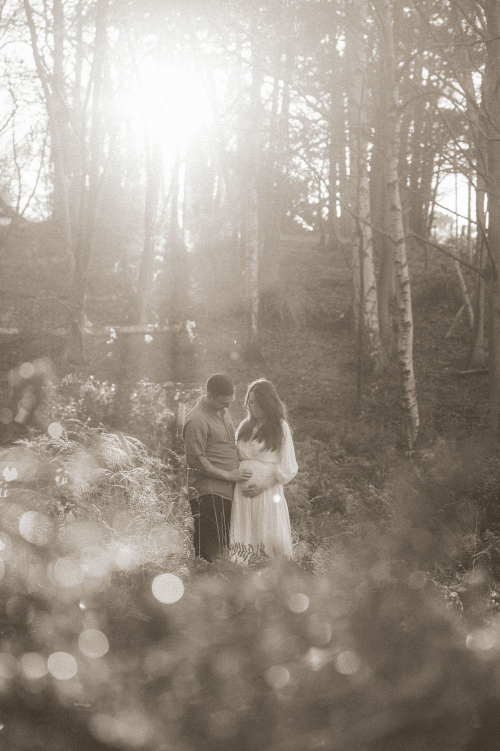 A romantic maternity photoshoot in a misty forest with dreamy bokeh effects in black and white.