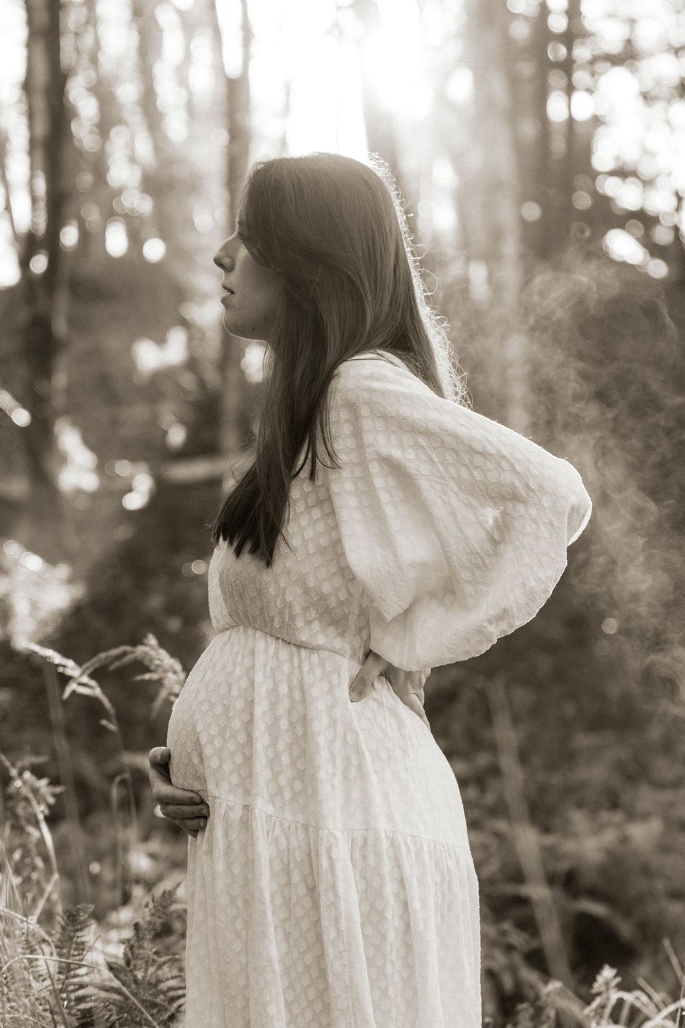 Dreamy black and white portrait of a flowing white dress among ferns in a forest setting.