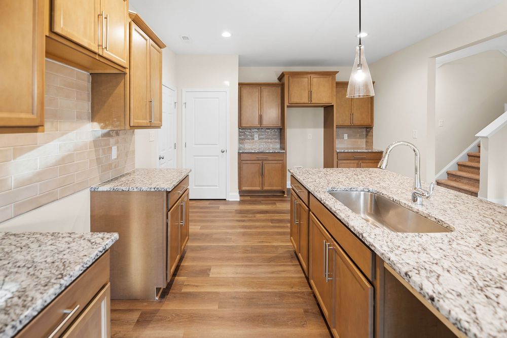 Modern kitchen interior with light granite countertops, honey oak cabinets and hardwood flooring in open concept layout.