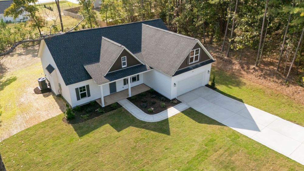 Aerial view of a modern residential home with white siding and dark roof surrounded by green lawn and trees.