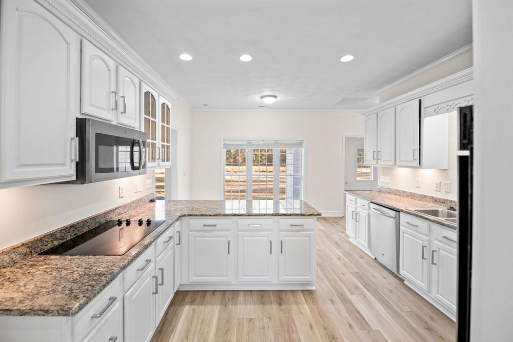 Modern white kitchen remodel features granite countertops, recessed lighting, and extensive cabinet storage space.