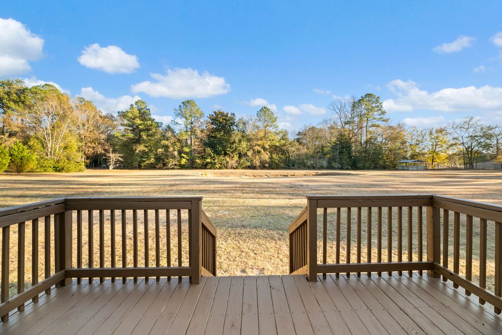 A wooden deck railing overlooking a scenic landscape with trees and blue sky on a sunny day.