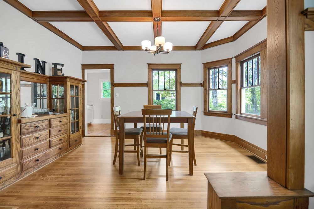 Modern craftsman style dining room with exposed wooden beams, hardwood floors, and large windows letting in natural light.