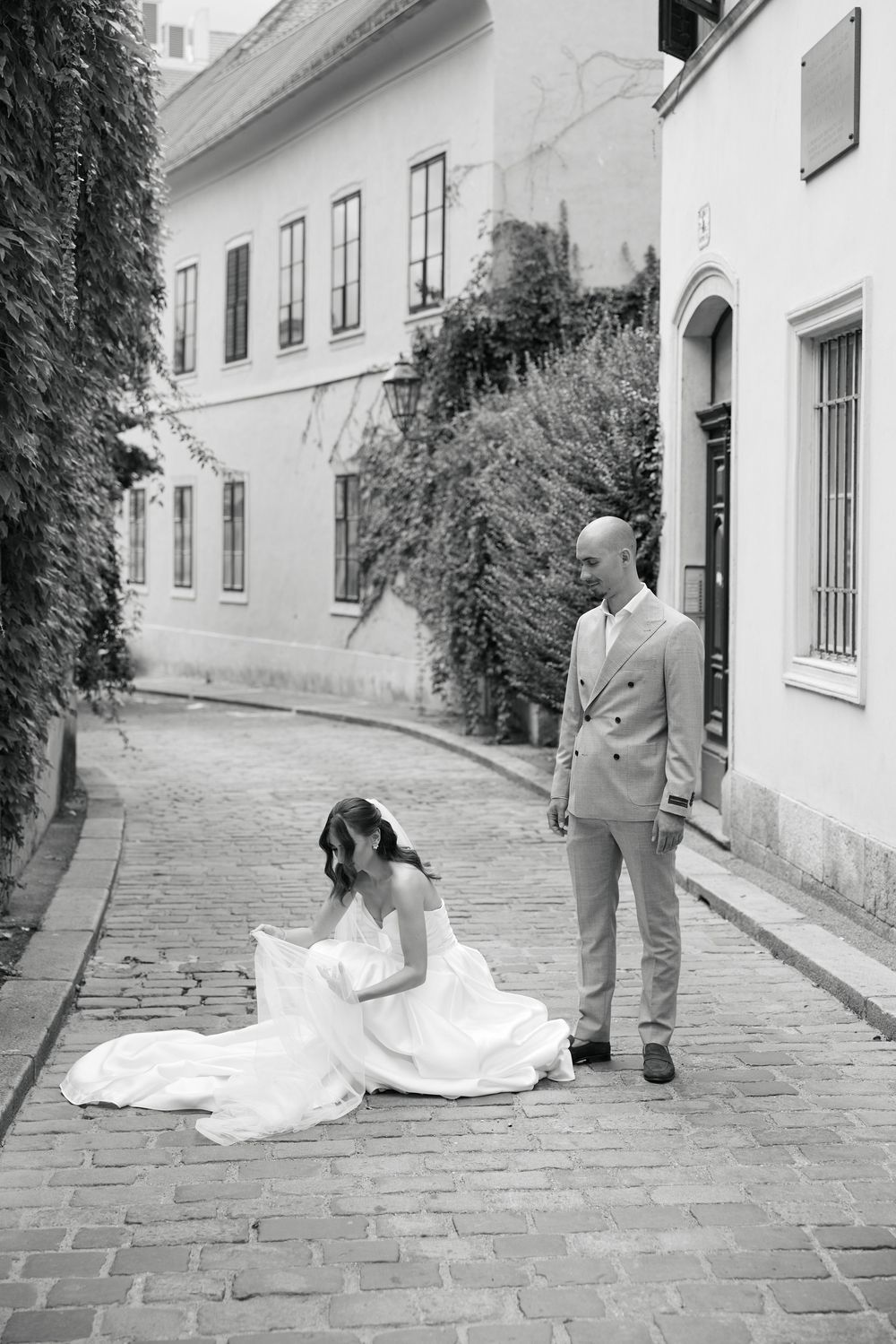 Black and white photo series of newlyweds on cobblestone street by white buildings.