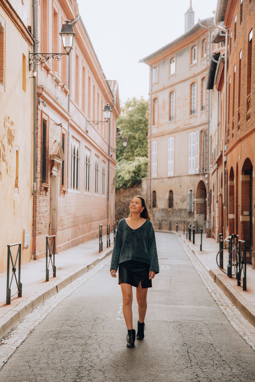 A young woman in a teal sweater and black mini skirt walks down a charming European cobblestone street.