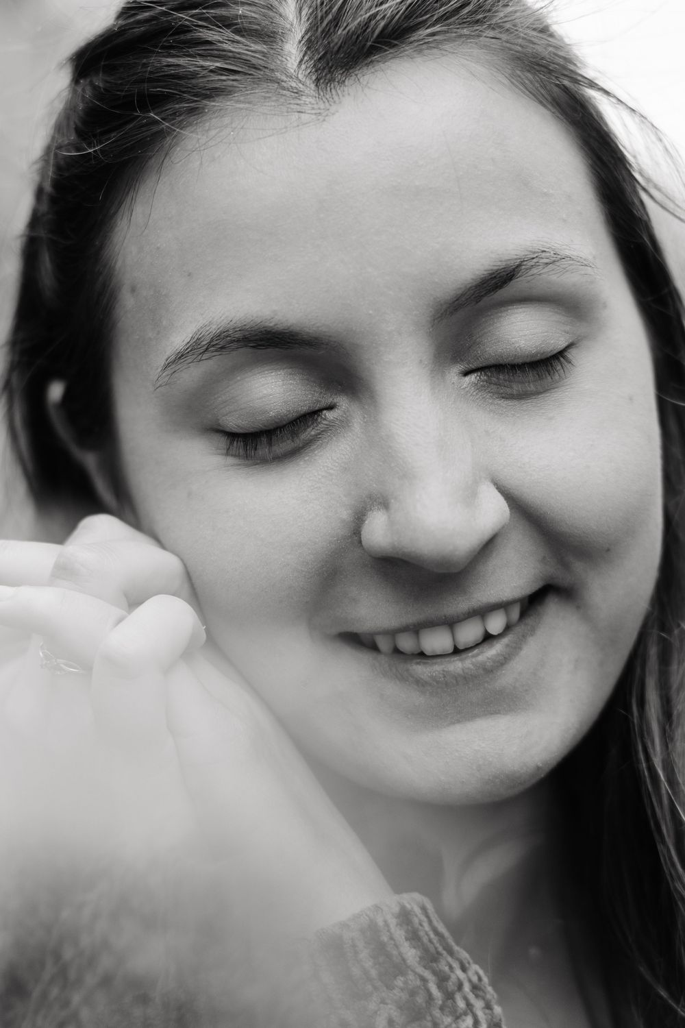 Black and white close-up portrait of smiling young woman with eyes closed, hand near face.