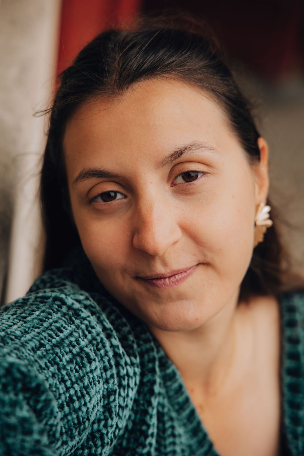 Close-up portrait of dark-haired woman in teal knit sweater smiling softly indoors.