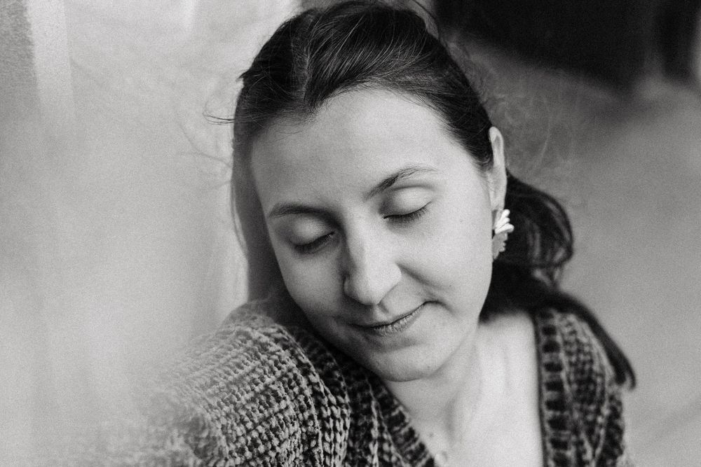 Black and white portrait of woman with dark hair and floral earring looking down pensively.