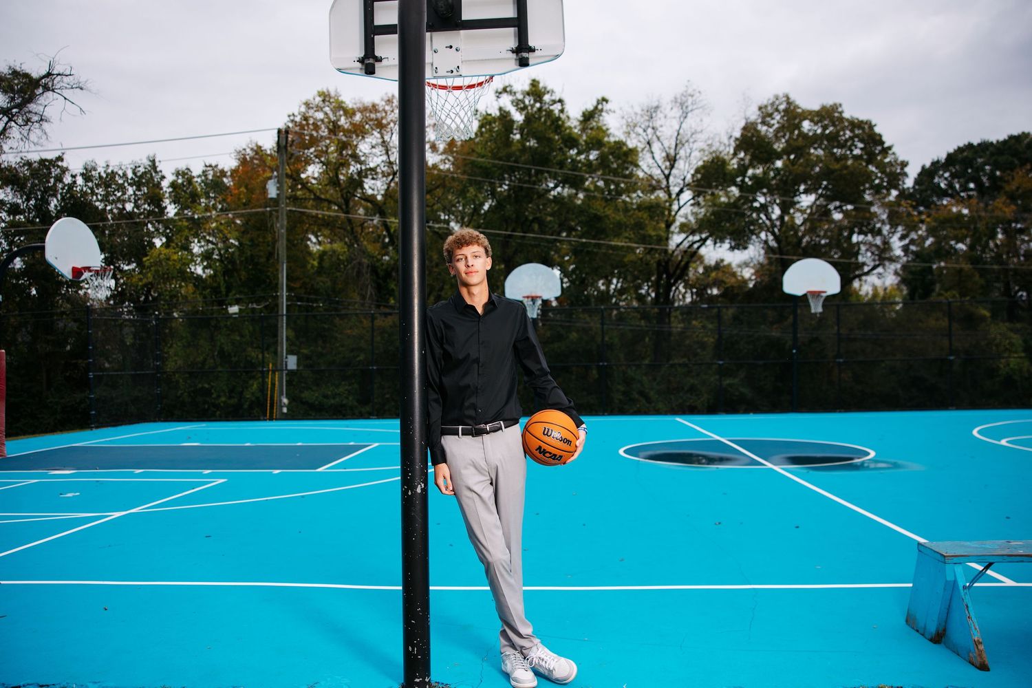 Basketball player dribbles on a bright turquoise outdoor court during a cloudy day.