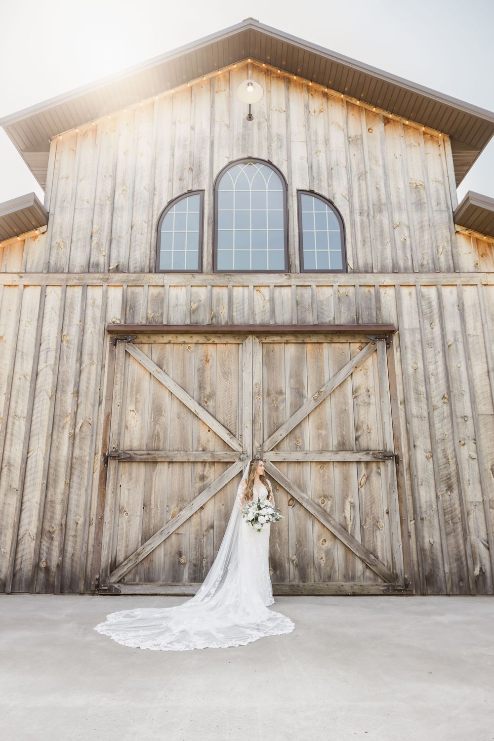 A white wedding dress train elegantly displayed against a rustic wooden barn door with arched windows.