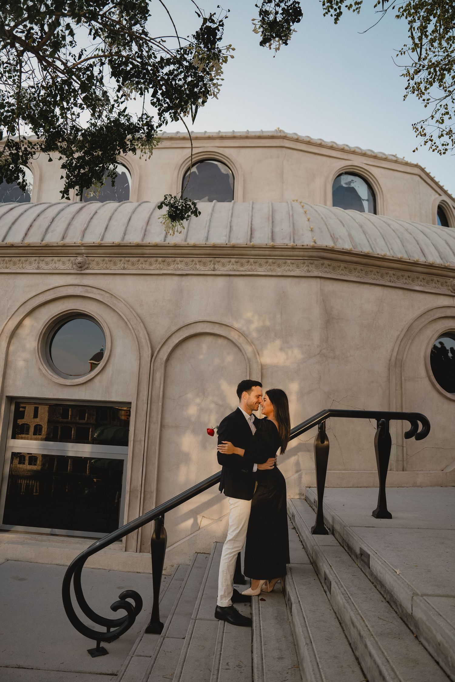 Couple posing on stone staircase in front of elegant architectural backdrop