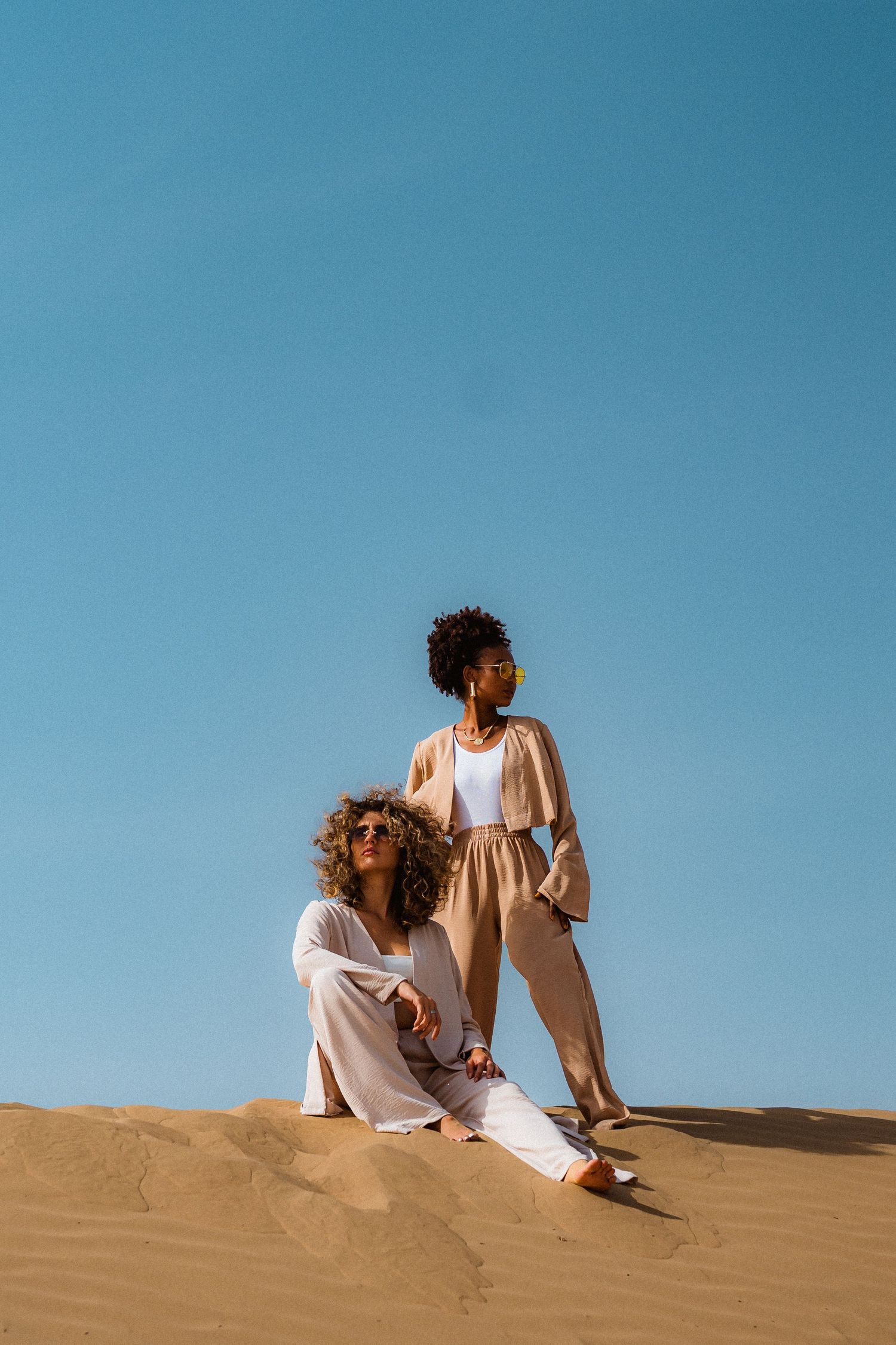Fashion portrait of woman seated on Dubai desert dunes under clear blue sky