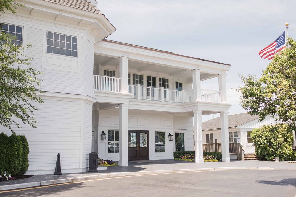 White colonial-style motel building with covered porches and balconies stretches across a sunny exterior view.