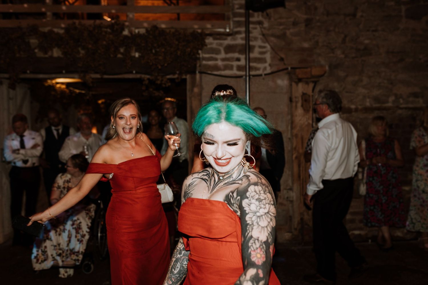 Group of wedding guests dancing and celebrating together on a dark dance floor in a rustic brick venue.