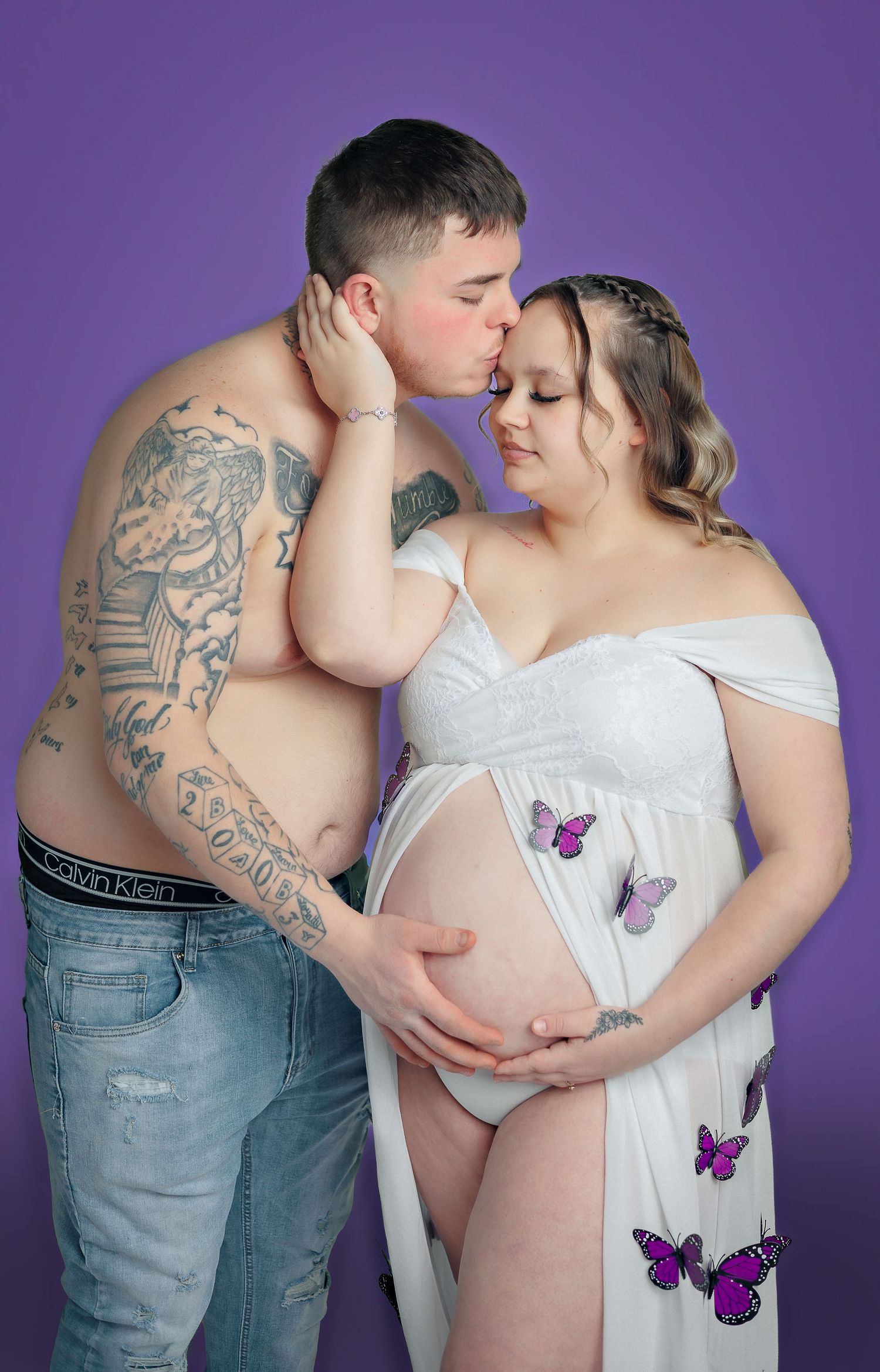 Maternity photoshoot with purple backdrop featuring butterfly dress and intimate poses.
