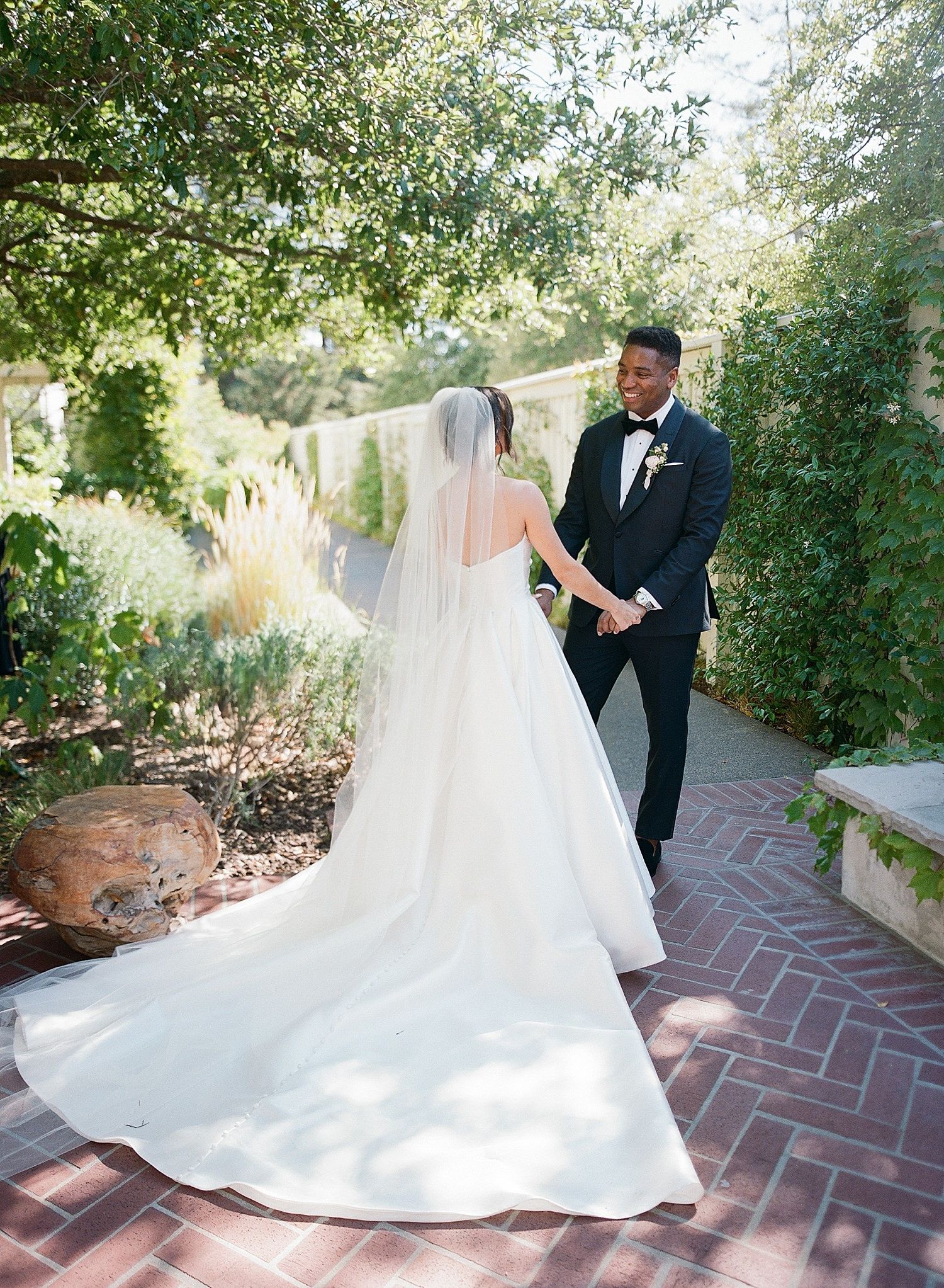 A wedding couple dances together on a brick pathway surrounded by lush garden greenery.