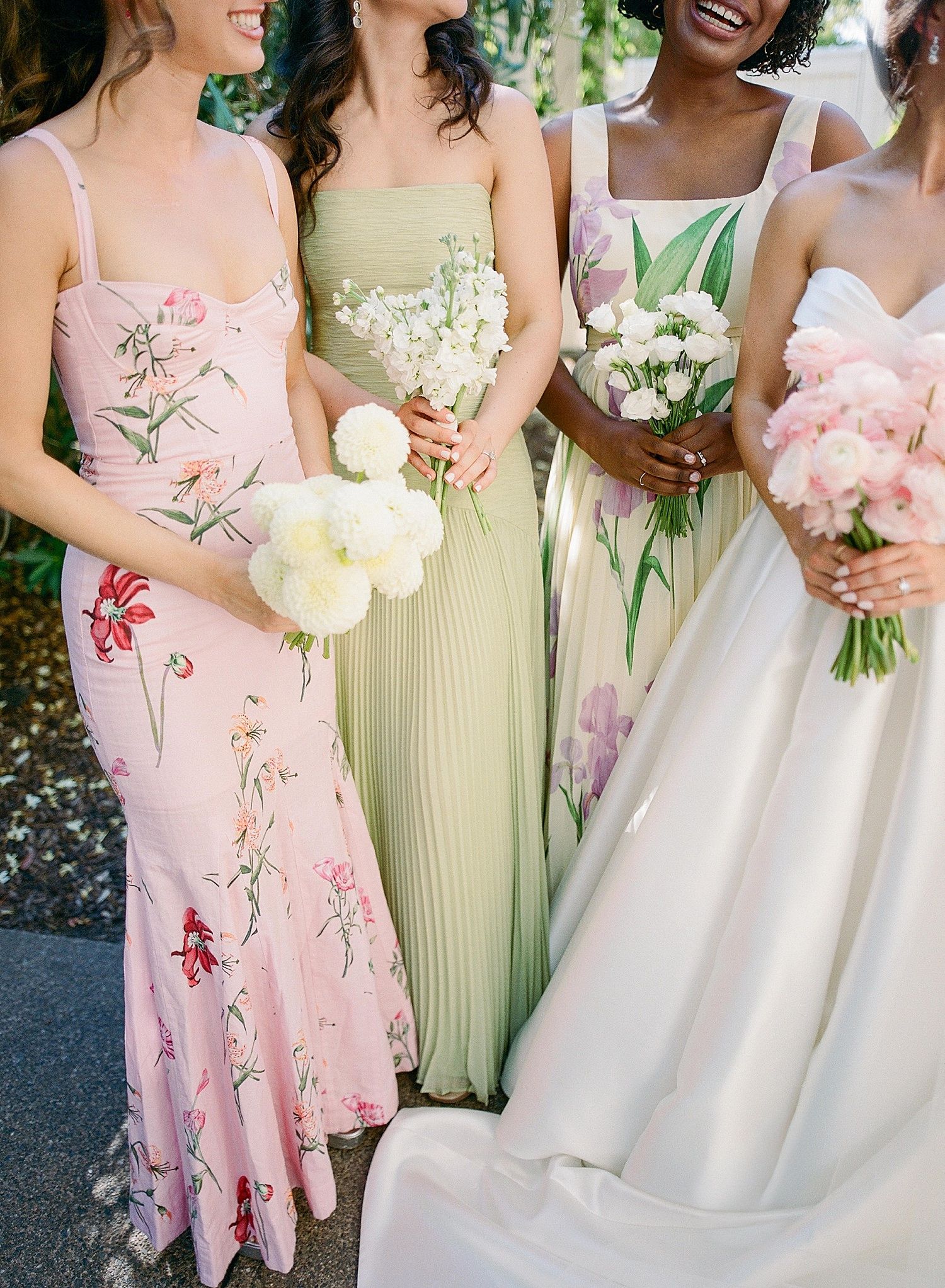 Bridesmaids in pastel pink and yellow dresses hold bouquets at an outdoor wedding celebration.