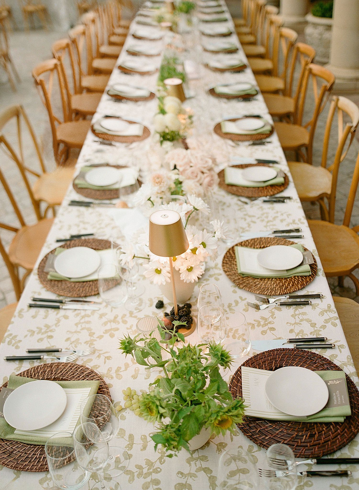 Long elegant dining tables set with white linens, woven chargers, and delicate greenery centerpieces for an upscale event.