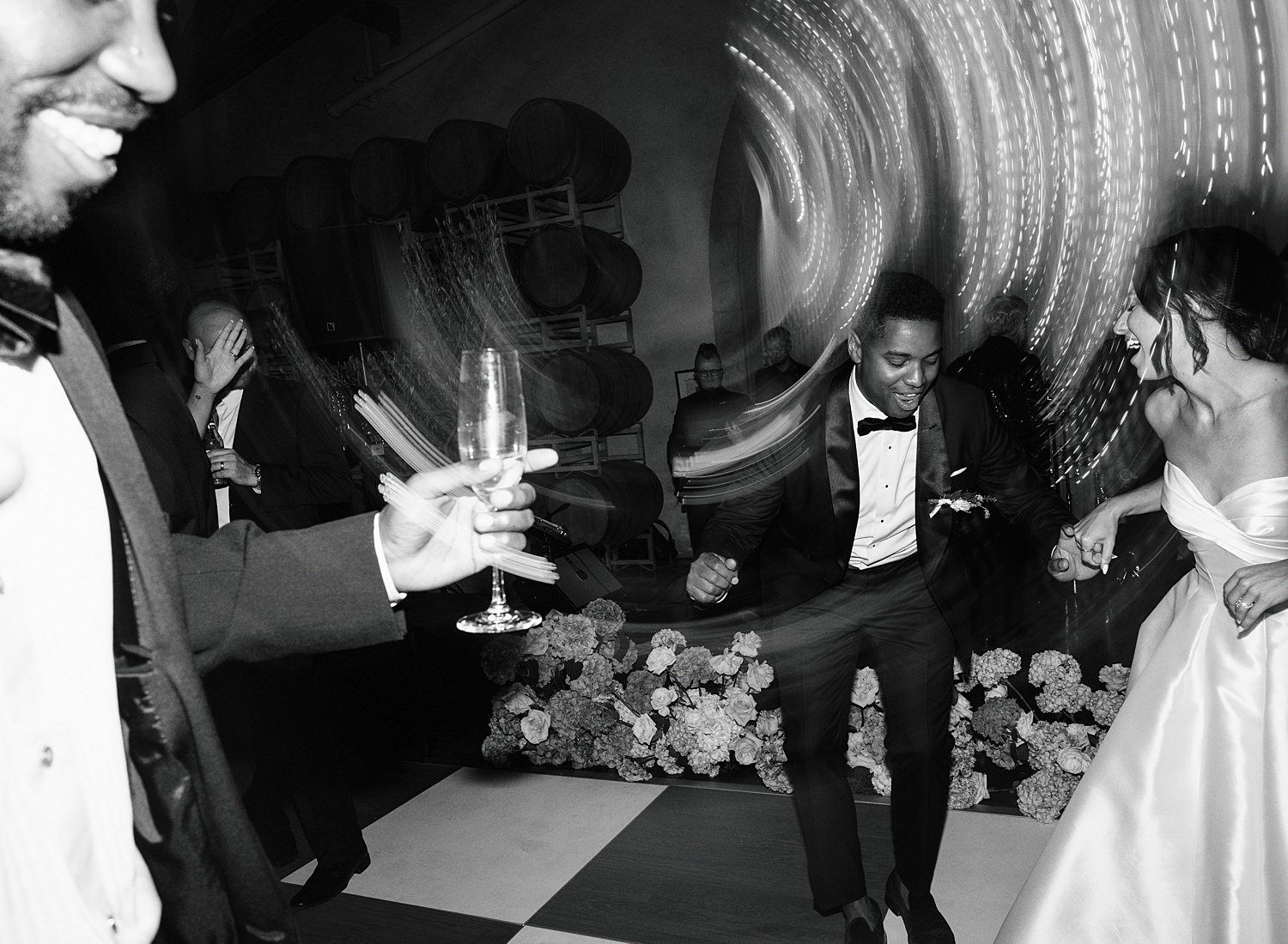 Black and white photo of wedding reception guests dancing and holding champagne glasses on a dance floor.