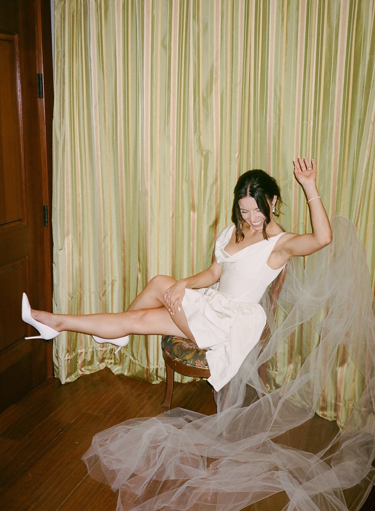 A dancer in a white dress performs a graceful falling sequence against striped curtains in a studio space.