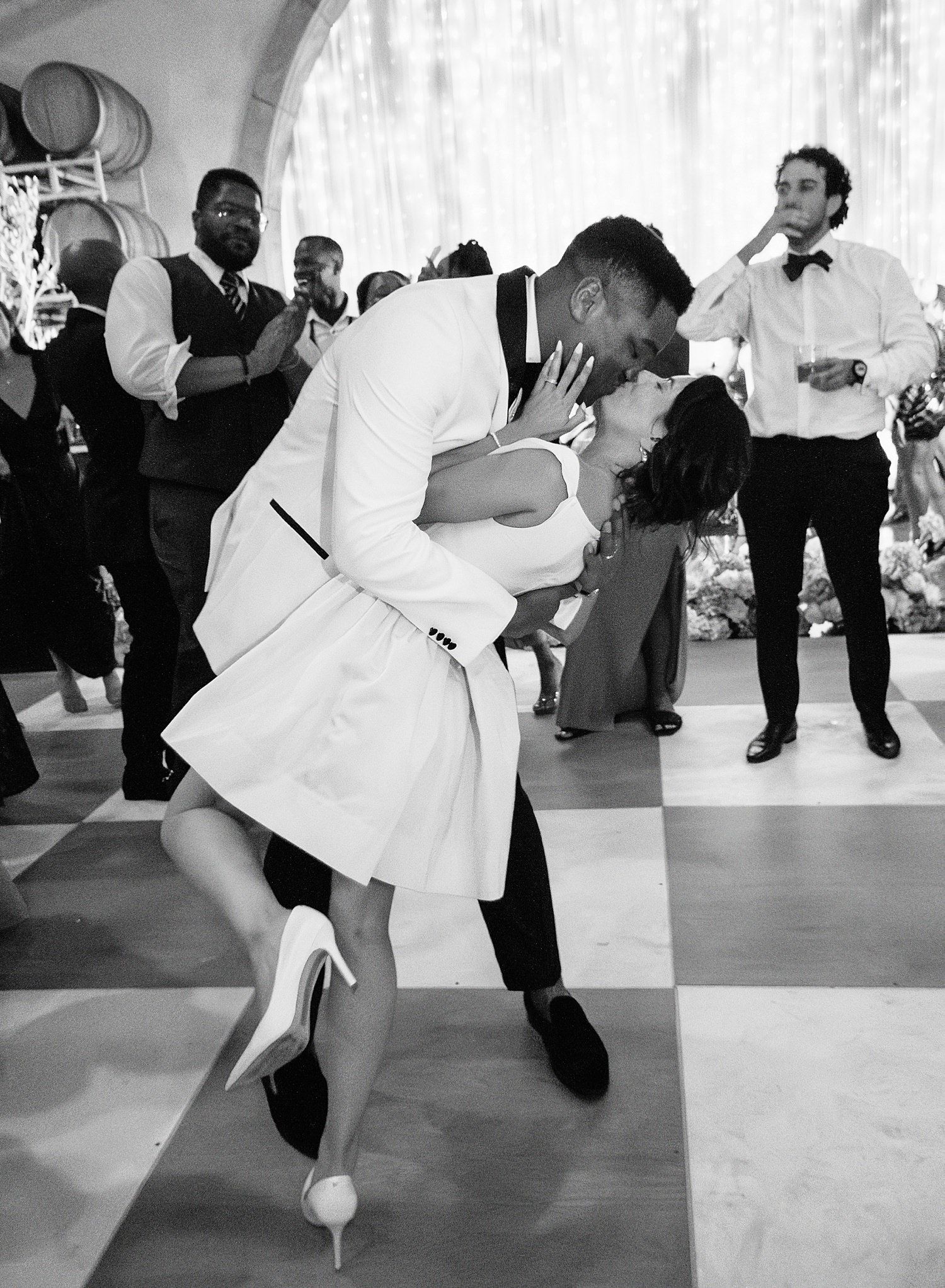 Dancers perform a dip move during a wedding reception on a black and white checkered dance floor.