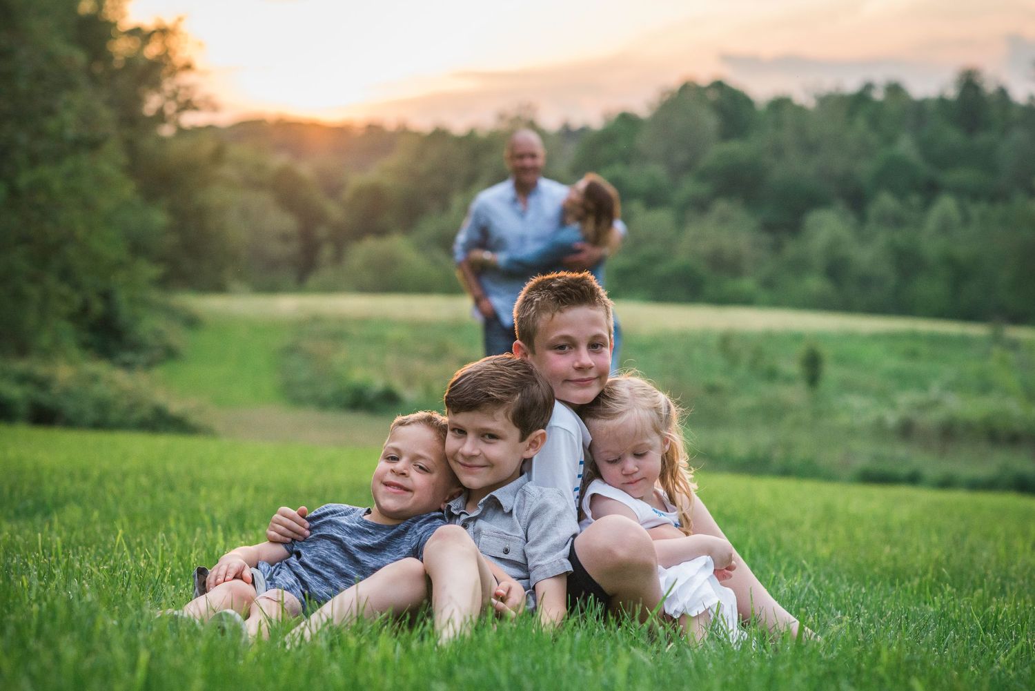 Family laying together on grassy hill during golden hour sunset.