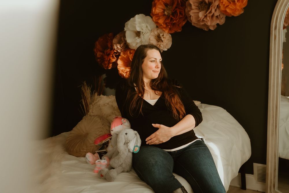 An expectant mother relaxes on a bed with floral decorations in the background.