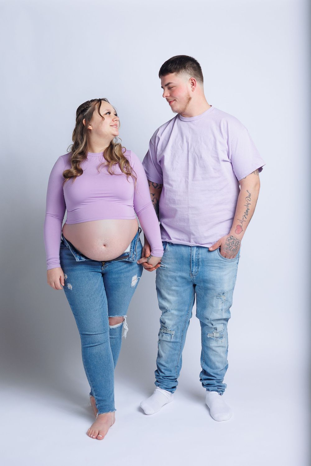A couple wearing matching purple shirts pose together during a maternity photoshoot.
