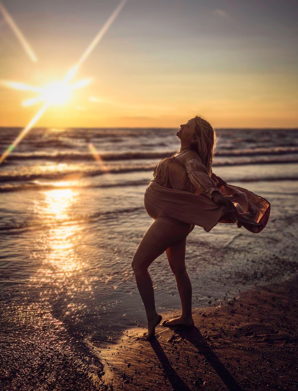 Silhouette of person exploring beach at sunset with dramatic sun flare.