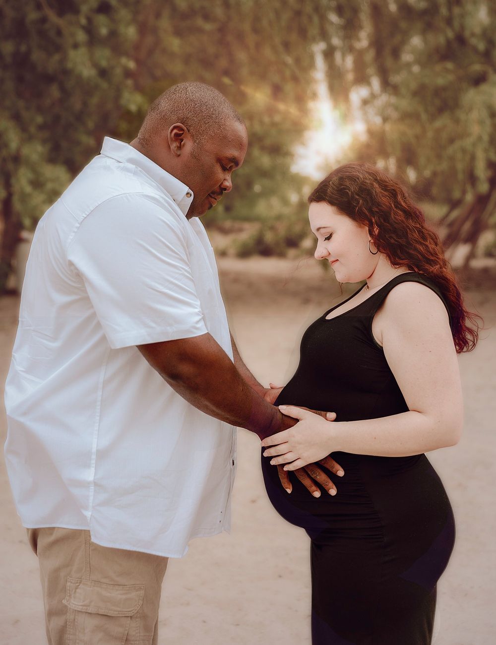 Couple shares tender moment during maternity photoshoot outdoors.