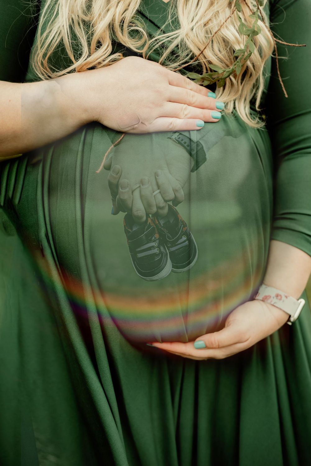 Hands frame a baby shoes reflection on a green maternity dress.