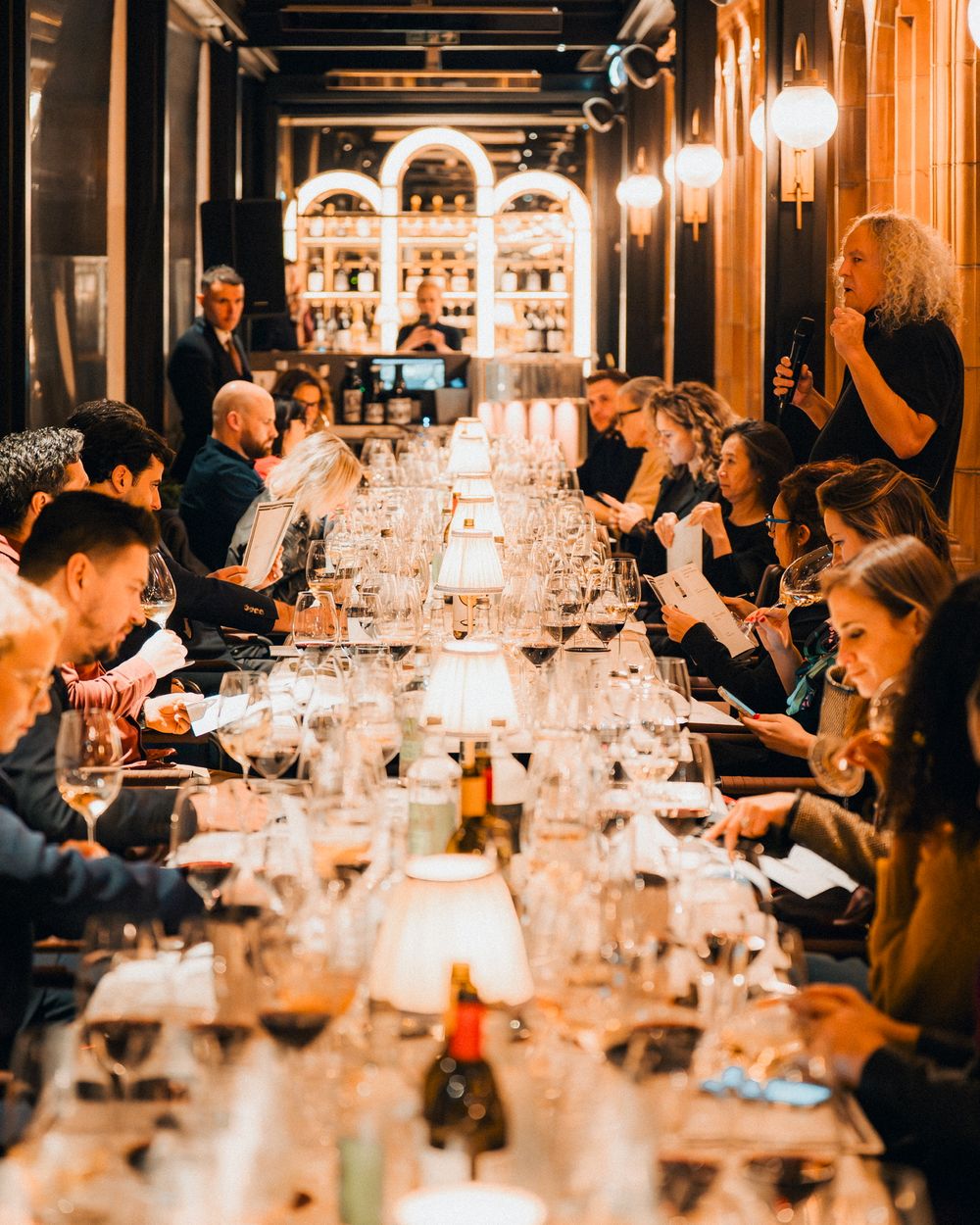 Candlelit dinner party with guests seated at a long table in an elegant restaurant setting.
