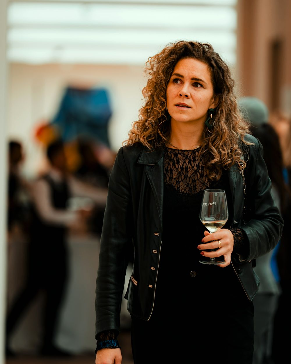 A woman in a black outfit holds a wine glass at an elegant evening event.